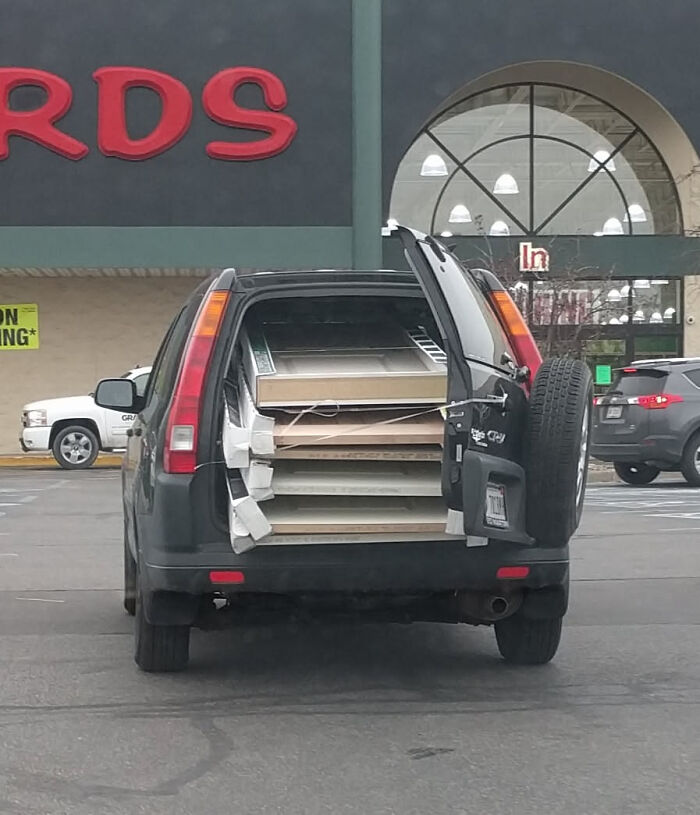 Black SUV with open trunk filled to the brim with wooden doors in a hilarious towing attempt