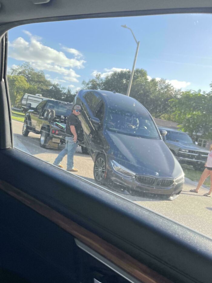 Black car standing nearly vertical while attached to a flatbed truck, a clear case of towing gone wrong.