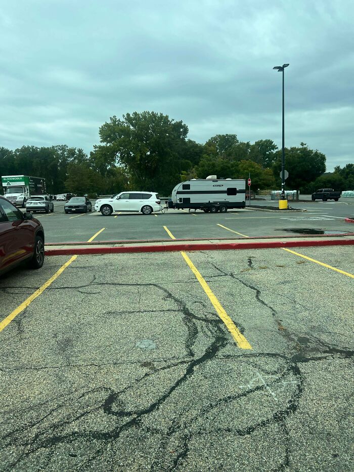 White SUV pulling a long camper trailer across multiple parking spaces, an example of towing gone wrong.