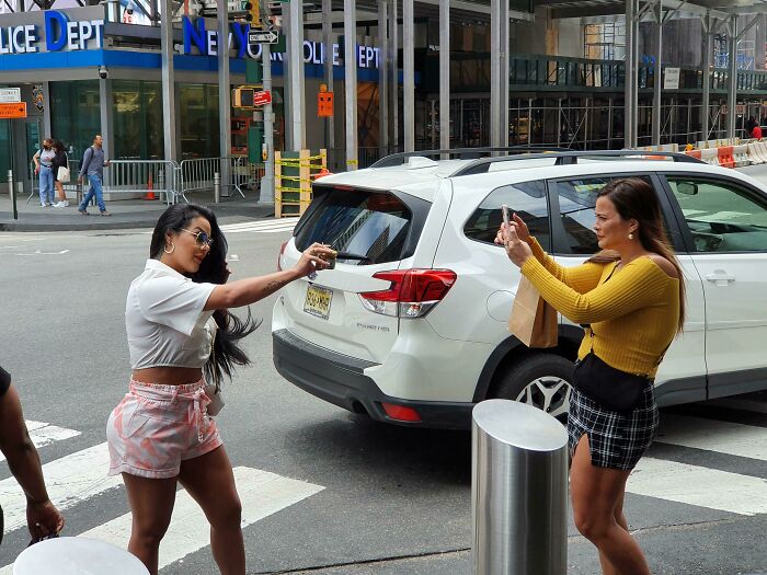Influencers taking photos of each other near a public street using smartphones.