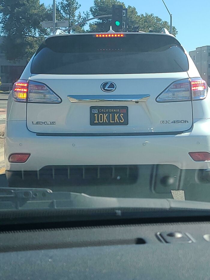 A rear view of a white Lexus car in public spaces featuring a custom California vanity license plate that reads 10K LKS.