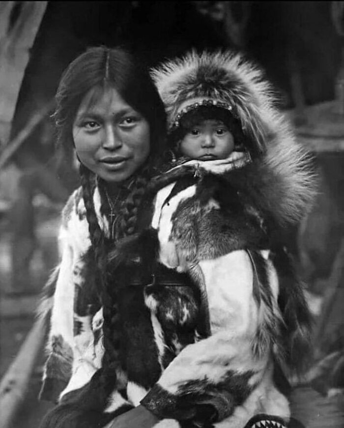 Historical photo of an Indigenous woman carrying a baby in fur clothing showing facts about the past.