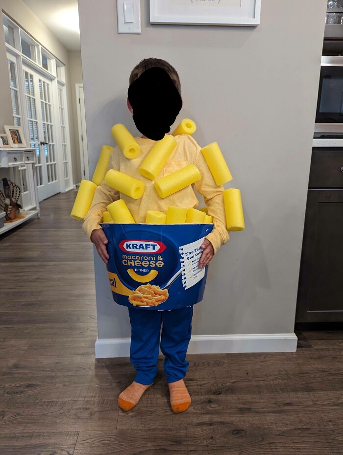 A kid wearing creative Halloween costumes shaped like a Kraft macaroni and cheese bowl with yellow pool noodles.