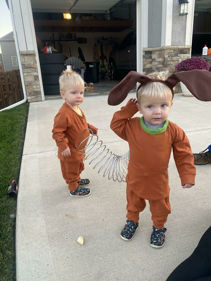 Twin toddlers dressed in Slinky Dog Halloween costumes connected by a metal spring.