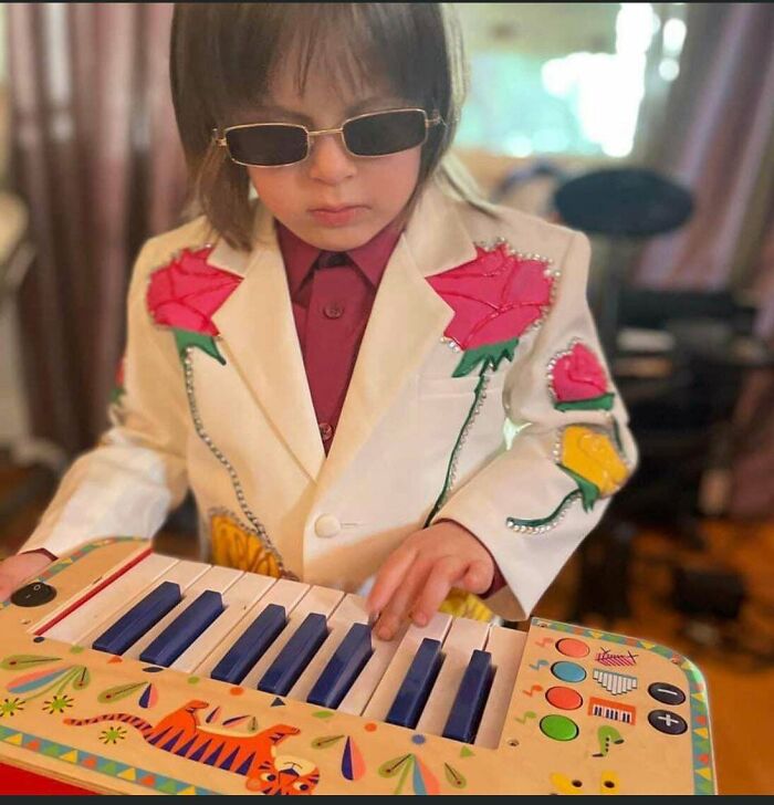 A kid dressed in a stylish white floral suit playing a toy piano for creative Halloween costumes