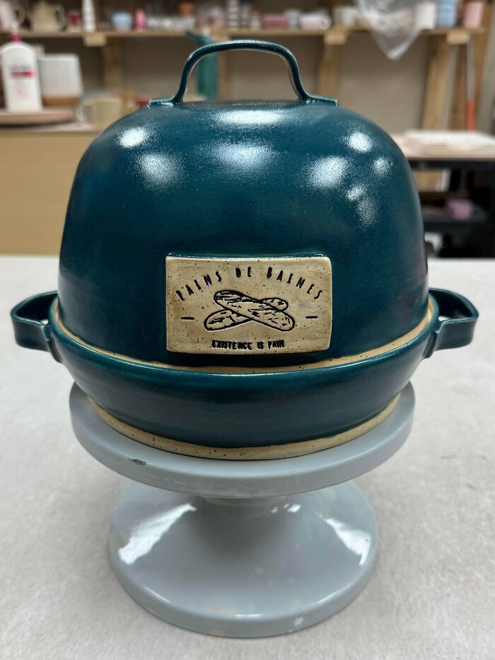 Teal ceramic bread baker showing pottery creations on a stand.