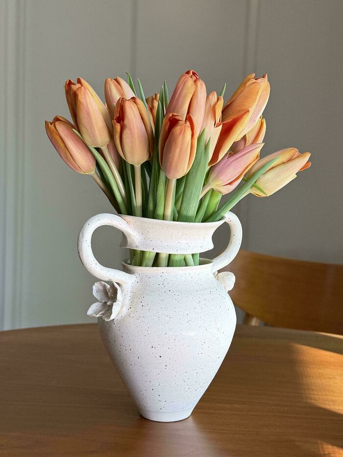 A speckled white ceramic vase with orange tulips, demonstrating elegant pottery creations.