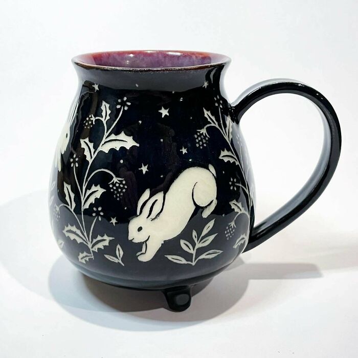 A dark ceramic mug featured among handmade pottery creations with rabbit and plant motifs.
