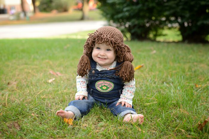 A baby sitting outdoors dressed in Cabbage Patch Kids Halloween costumes with yarn hair
