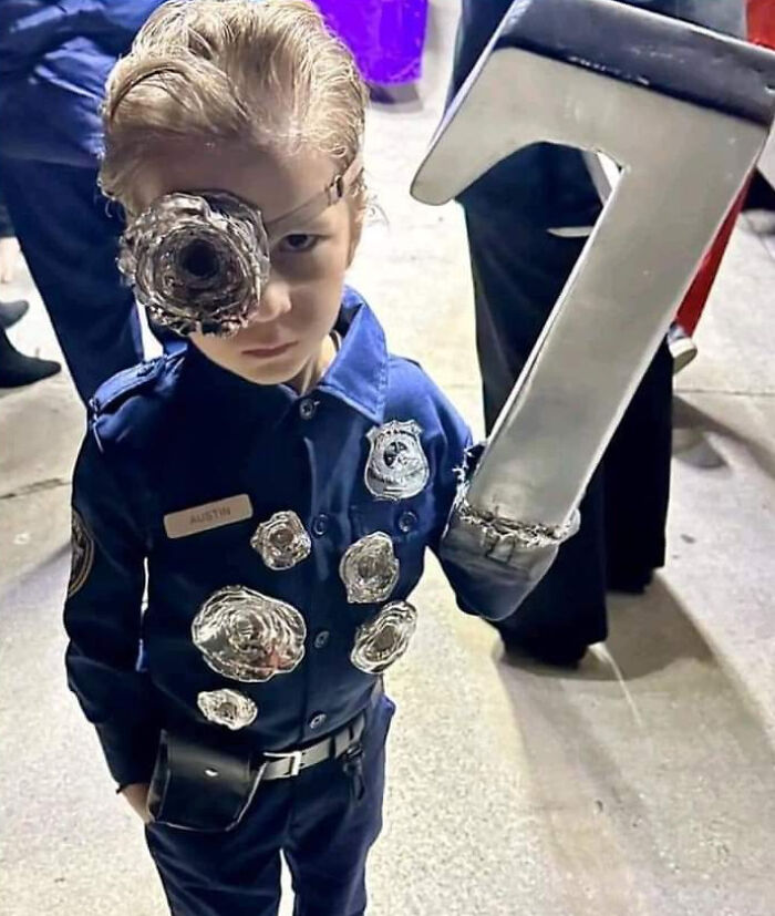 A young child wearing a detailed T-1000 police Halloween costume with liquid metal metallic details.