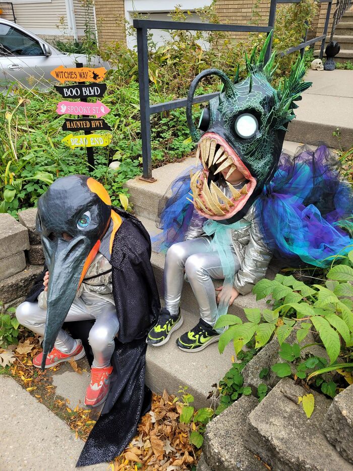 Two kids wearing creative sea creature Halloween costumes sitting together on outdoor steps