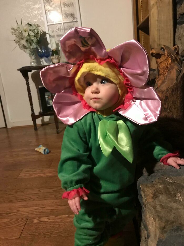 A cute baby wearing a bright pink and green flower Halloween costume indoors.