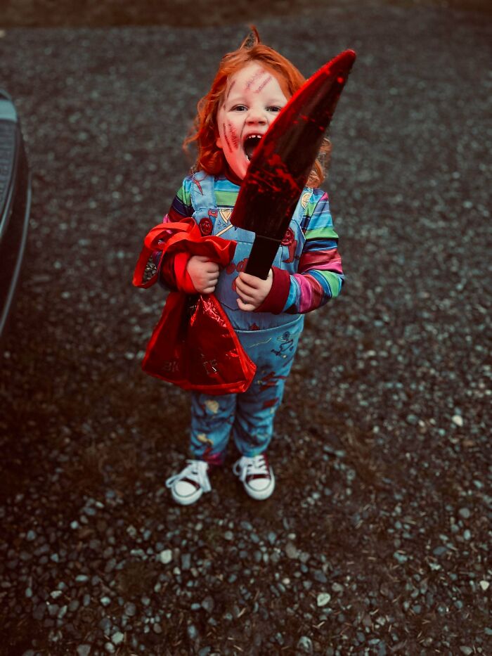 A child wearing a creepy horror movie Chucky style Halloween costume with a large fake knife.