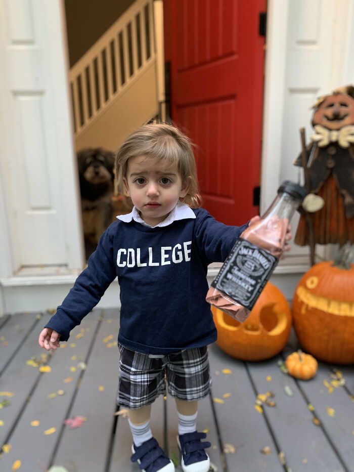 Toddler dressed in an Animal House college shirt holding a toy bottle as creative Halloween costumes for kids.
