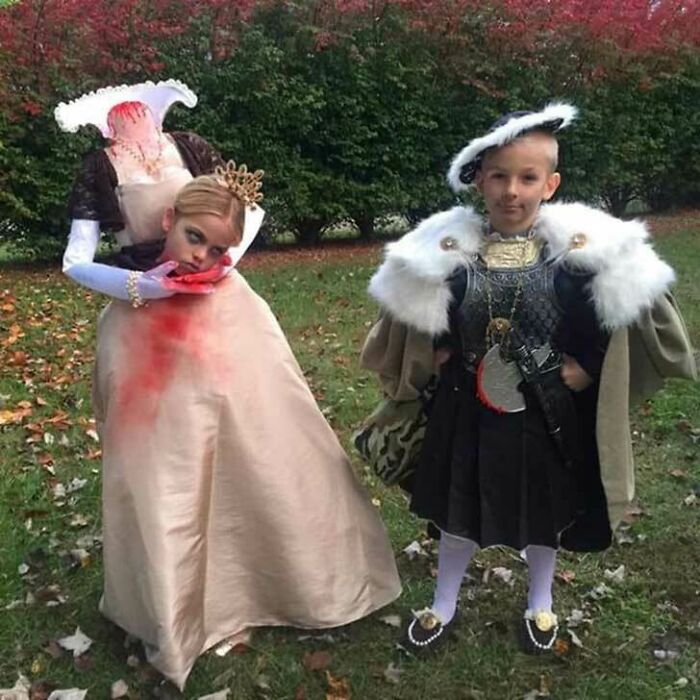 Two children wearing elaborate headless queen and king kids Halloween costumes outdoors.