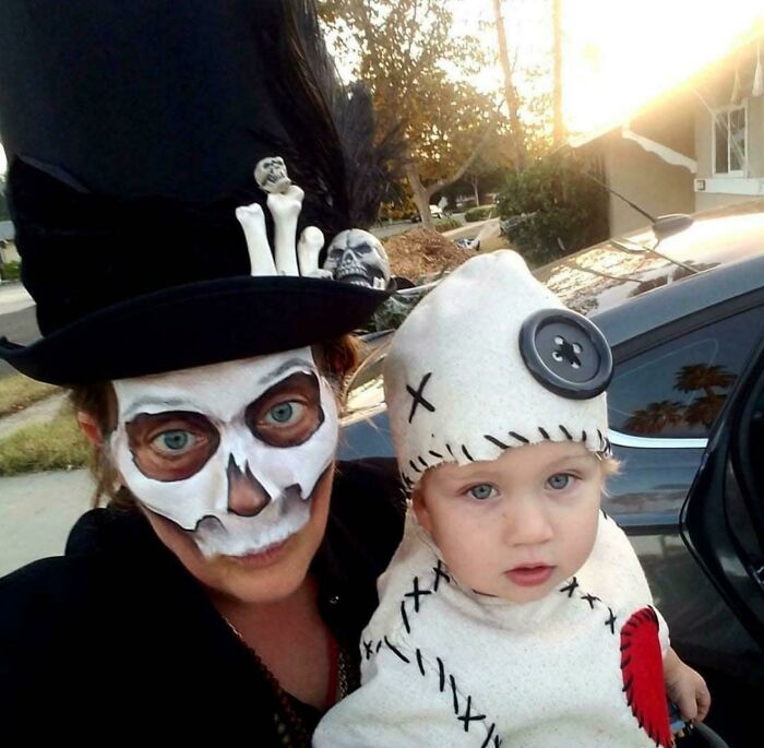 A parent with skull face paint next to a toddler in creative Halloween costumes including a voodoo doll outfit.