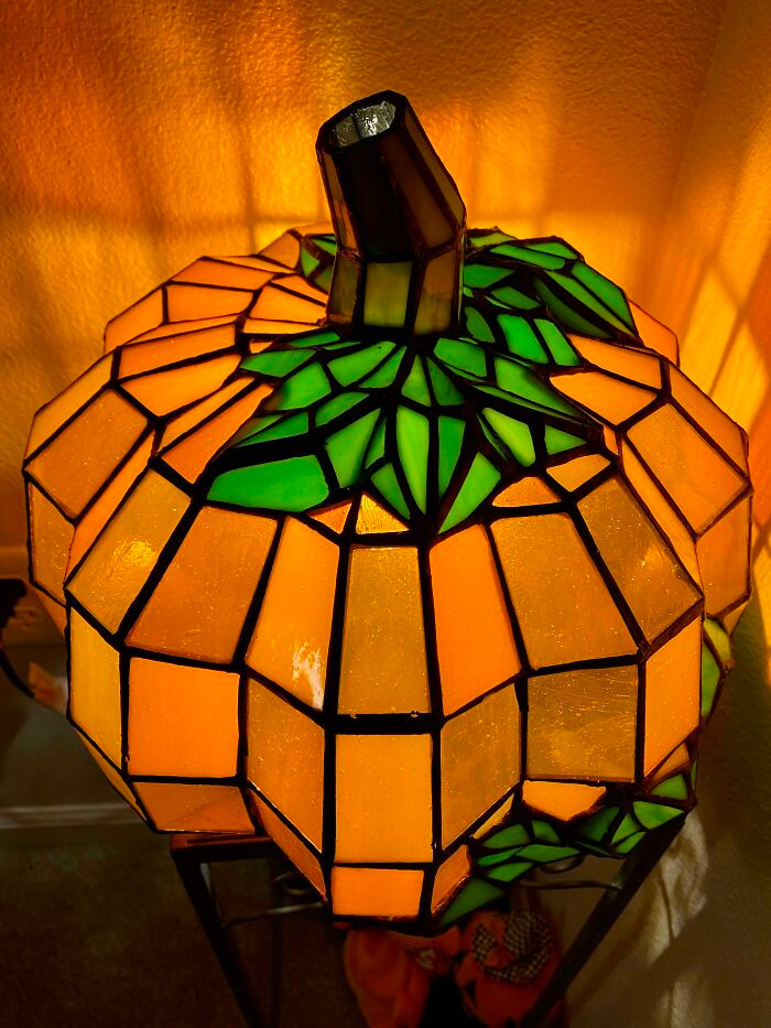Illuminated stained glass pumpkin lamp glowing in warm orange and green tones for Halloween.