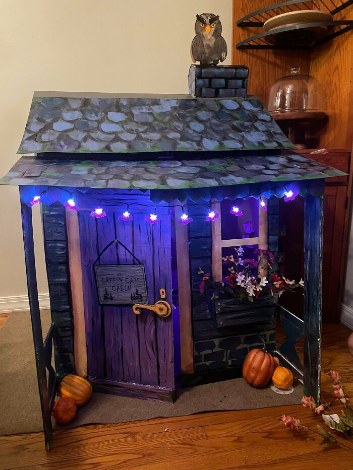 Miniature playhouse styled as a spooky cabin with string lights and small pumpkins for Halloween decor.