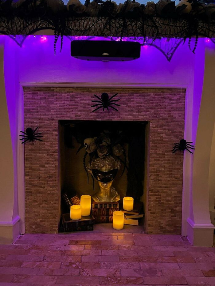 Spooky fireplace filled with glowing candles, a golden bust, and fake spiders for Halloween.