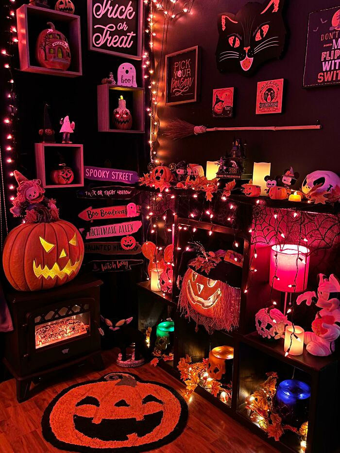 A room filled with spooky Halloween decor, orange lights, glowing jack-o-lanterns, and black cat wall art