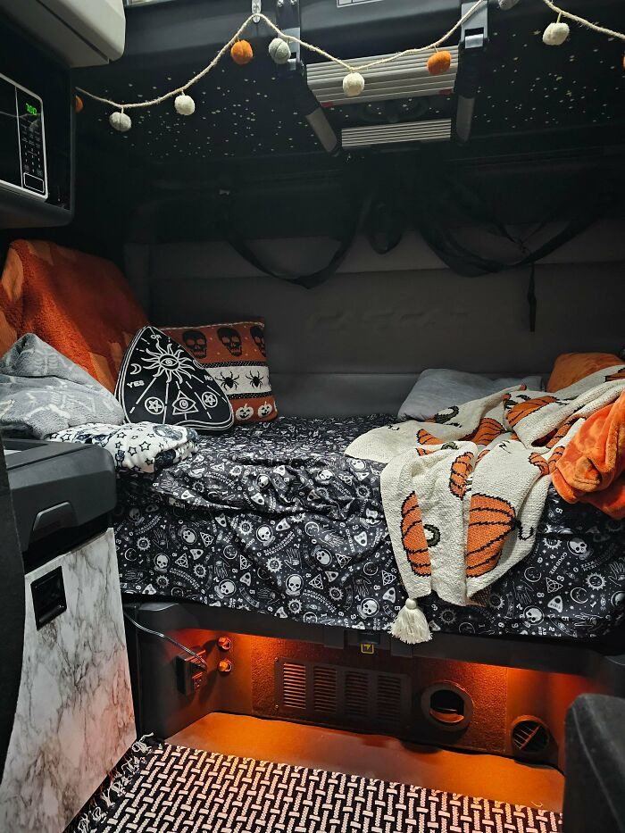 A semi-truck sleeper cab cozy bed area styled with spooky Halloween bedding, pillows, and string lights