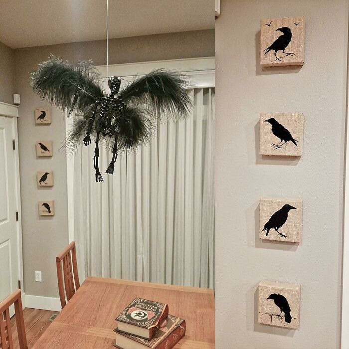 A flying winged skeleton hanging over a table surrounded by crow wall art for a Halloween home decoration setup