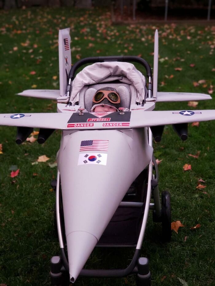 A baby sitting in a fighter jet stroller costume for creative kids Halloween costumes.