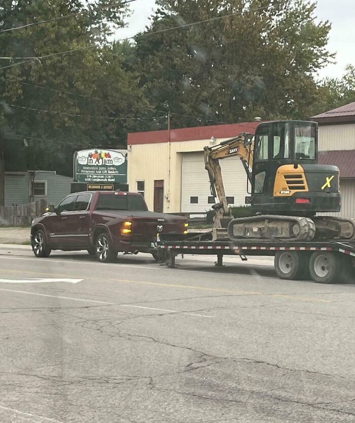 Pickup truck towing an oversized excavator on a flatbed trailer, an example of towing gone wrong.