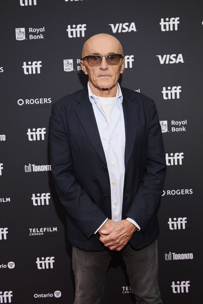 Filmmaker Danny Boyle wearing glasses and a navy suit blazer posing on a TIFF red carpet