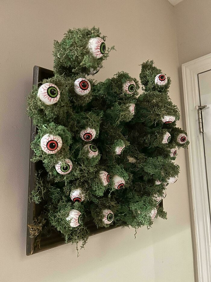 Creepy Halloween wall decor with artificial moss filled with numerous realistic fake eyeballs.