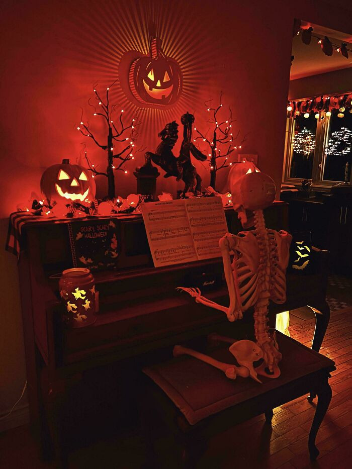 Halloween decor featuring a skeleton seated at an upright piano surrounded by lit jack-o-lanterns.