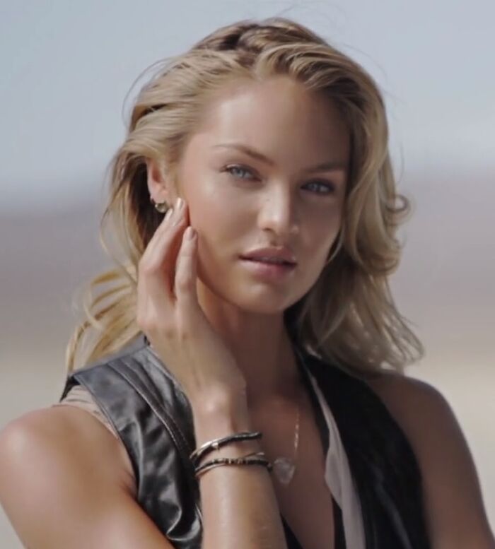 Close-up portrait of model Candice Swanepoel touching her cheek with styled blonde hair and subtle makeup