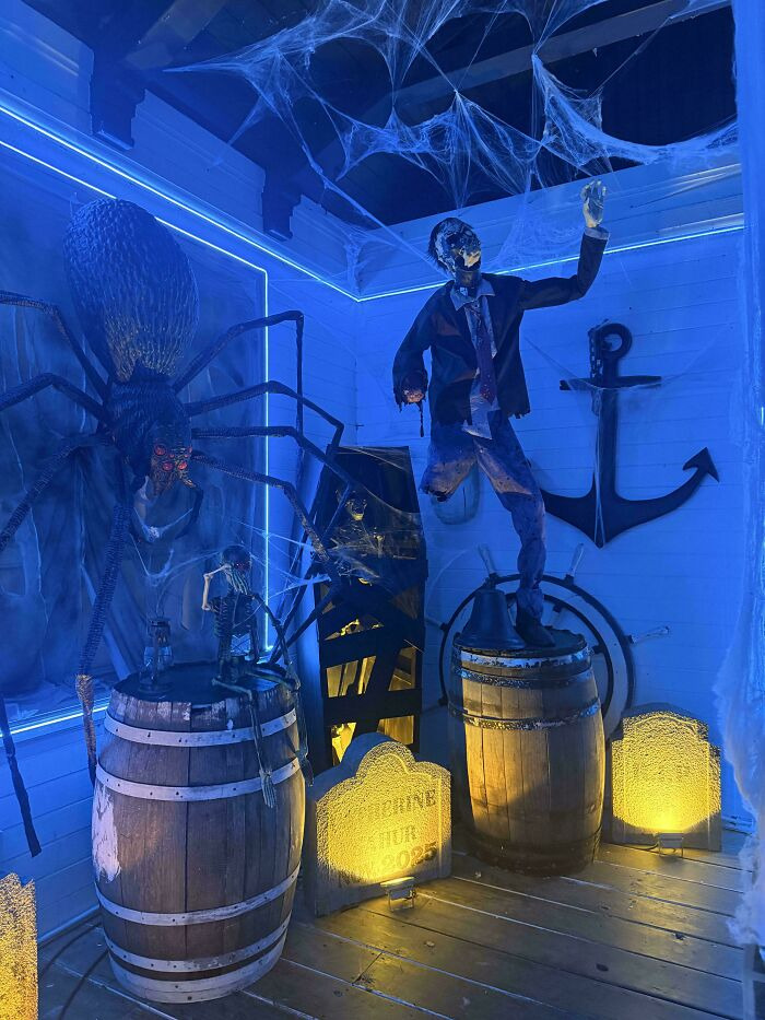 Spooky Halloween room with a giant spider, zombie figure, wooden barrels, cobwebs, and blue lighting.