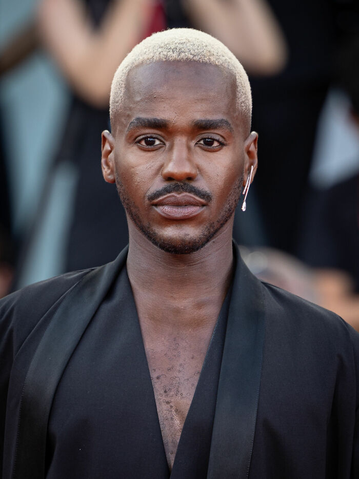 Actor Ncuti Gatwa with blonde buzz cut hair looking at the camera on the red carpet