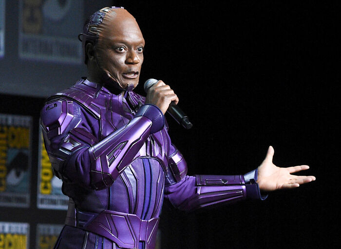Actor Chukwudi Iwuji speaking into a microphone on stage while wearing a purple sci-fi costume.