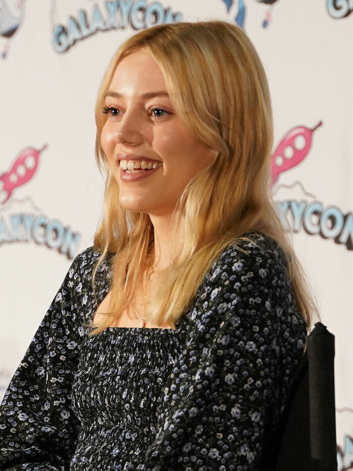 Actress Grace Van Dien smiling in a dark floral dress at an event