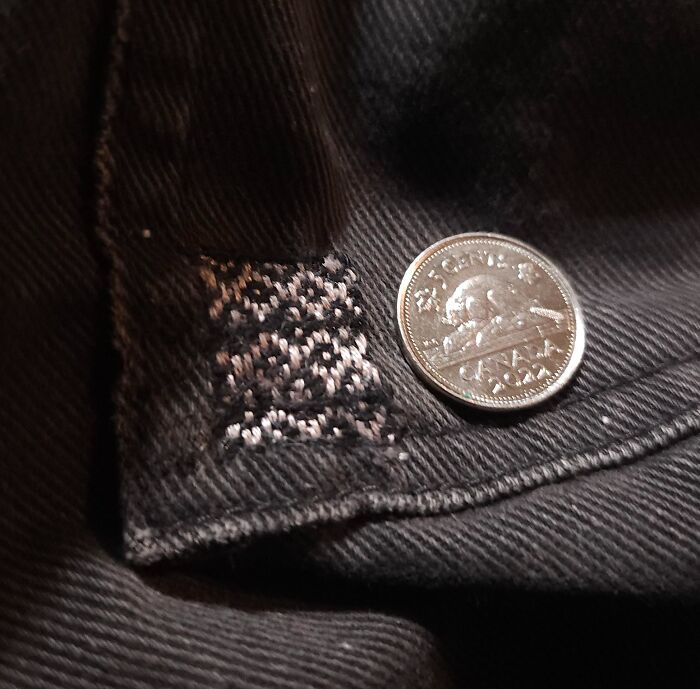 Close-up of a small visible mending stitch next to a coin, demonstrating how creativity can save money.