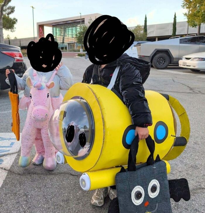Children wearing elaborate homemade costumes in a parking lot, representing wholesome pics of dads supporting their kids.