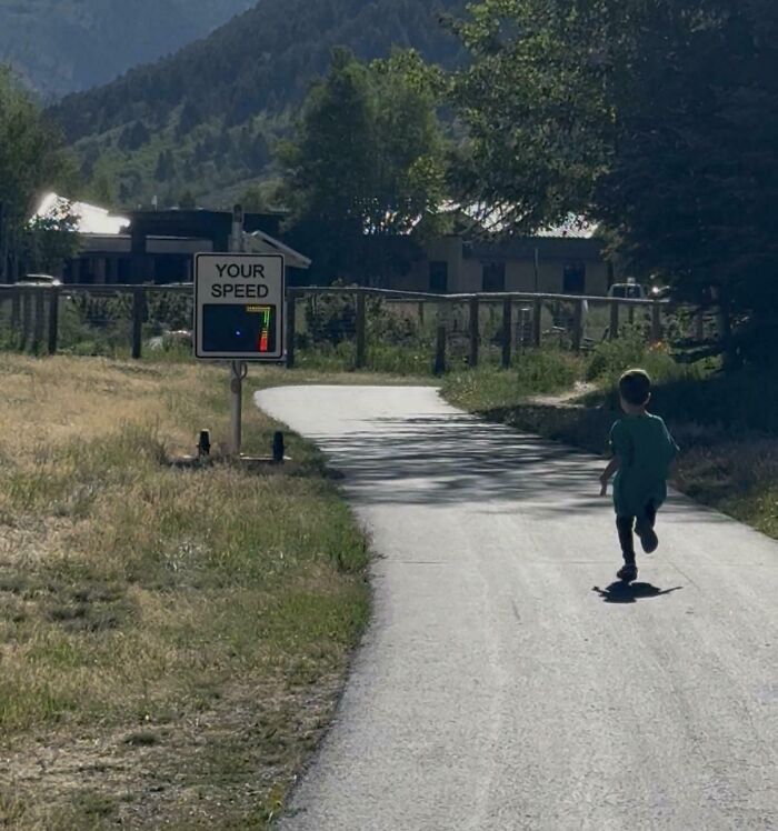A young child running along a path towards a speed radar sign, showing wholesome pics of dads parenting.