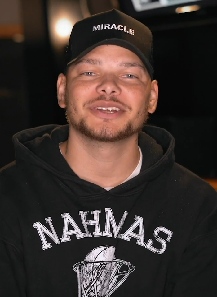 Country singer Kane Brown smiling in a black Miracle hat and hoodie