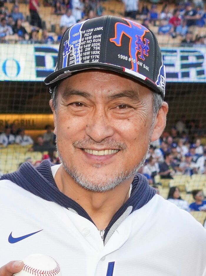 Actor Ken Watanabe smiling while wearing a baseball cap at a stadium