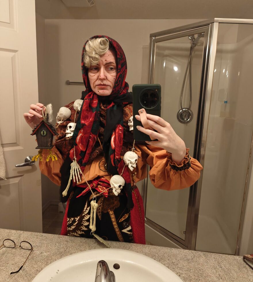 Woman taking a bathroom selfie dressed as a witch with skull decor for a creative Halloween costume idea.
