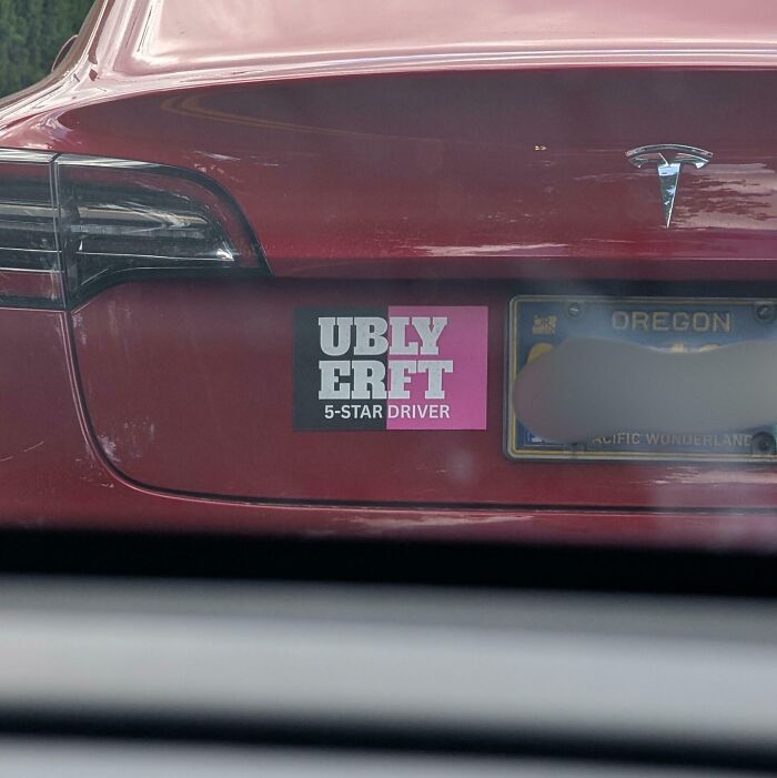 A bumper sticker with poorly aligned text on a red Tesla car, showcasing terribly designed signs.