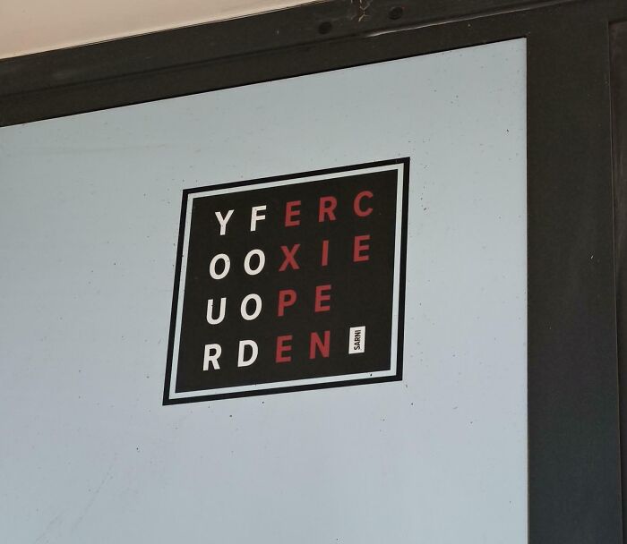 A terribly designed sign on a square window decal with confusing jumbled letters in black and red