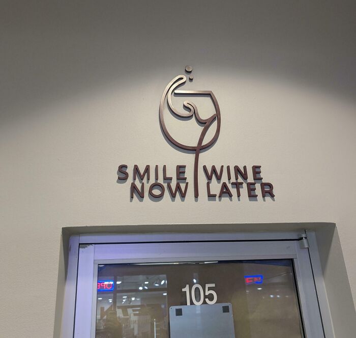 A terribly designed sign above a door that reads Smile Now Wine Later in a confusing layout