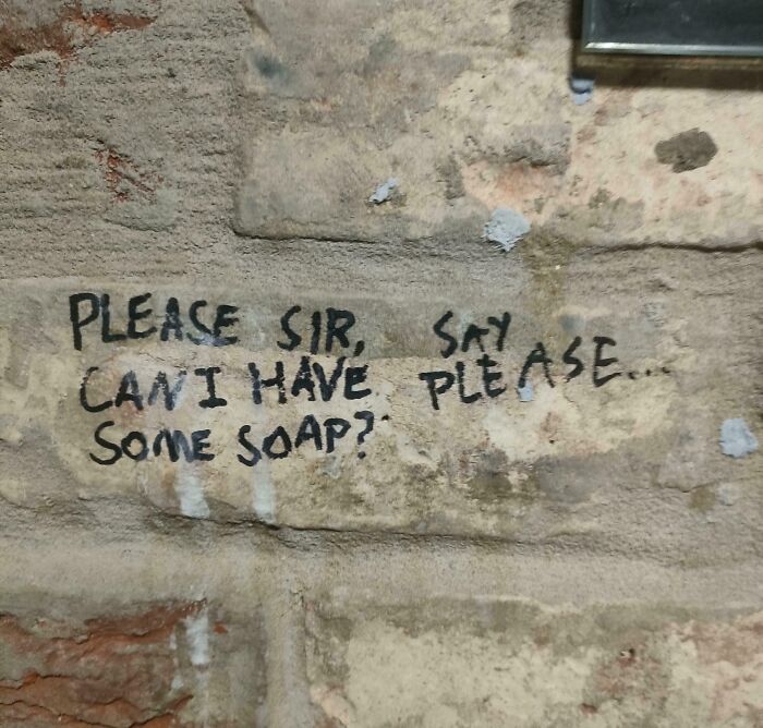Handwritten text on a stone wall asking for soap, featuring confusing and terribly designed signs layout.