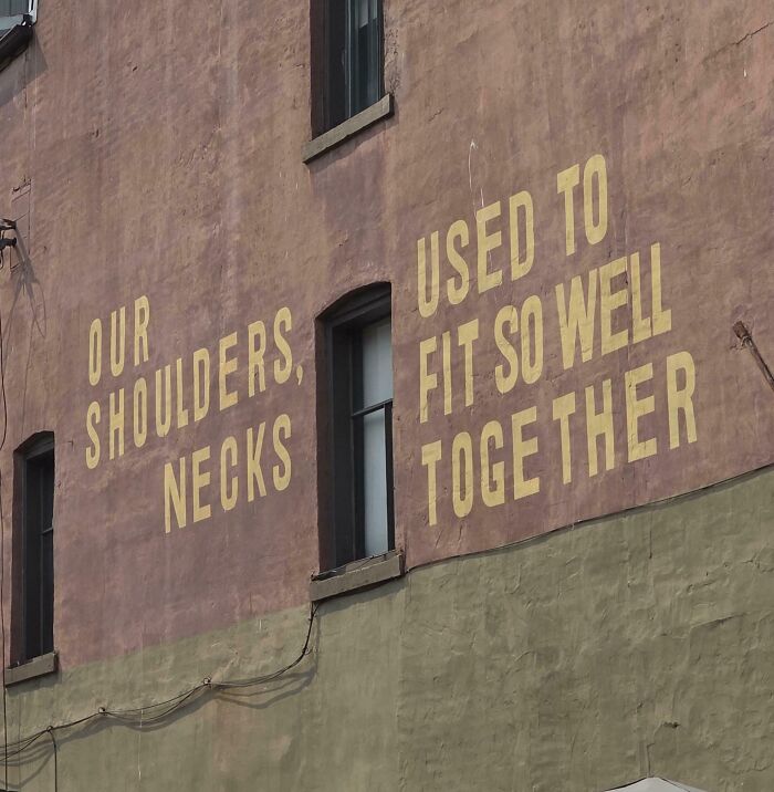 A terribly designed sign painted on a brick wall with confusingly layout text reading Our Shoulders Necks