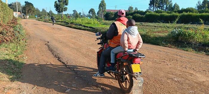 Rear view of a man riding a motorcycle on a dirt road with his child, showcasing wholesome pics of dads.