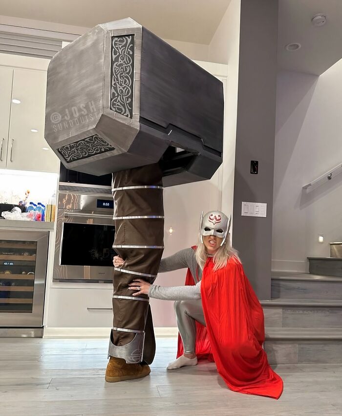 Woman in Thor costume posing next to a giant Mjolnir hammer for funny cool Halloween couples costumes