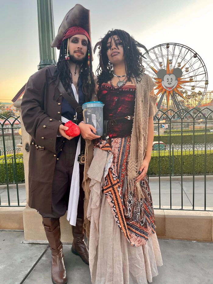 A couple dressed in Pirates of the Caribbean inspired Halloween couples costumes near a Ferris wheel